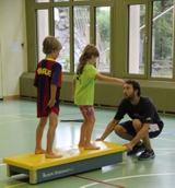 Zwei Kinder balancieren auf einem Schwedenbalken in einer Turnhalle.