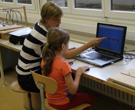 Doktorandin erklärt einem Mädchen eine Aufgabe am Computer.