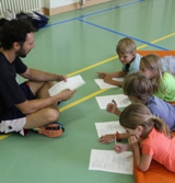 Der Studienleiter stellt Kindern, die auf Matten liegen, Aufgaben.