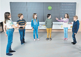 Kinder in der Schule spielen mit einem Ball vor einer Wandtafel.