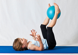 Ein Kind liegt auf dem Rücken und hält einen Ball mit seinen Füssen in die Luft.