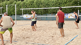 Personen üben den Umgang mit einem Ball auf einem Beachvolleyballfeld.